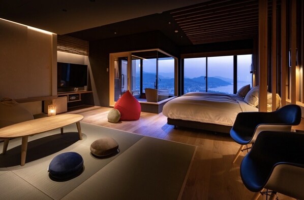 A modern bedroom with a large bed, a TV, and a view of the city and mountains.