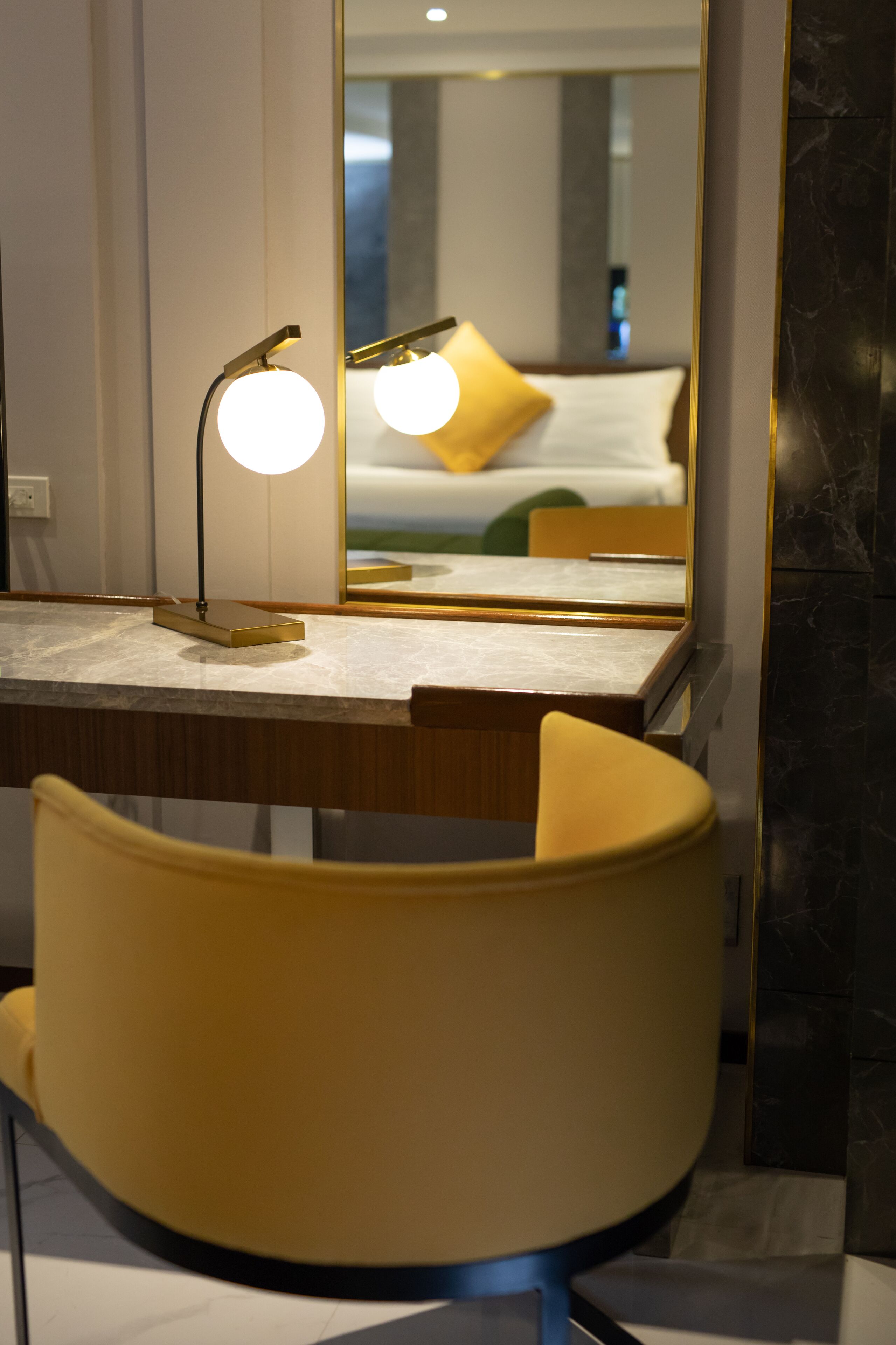 Ein modernes Hotelzimmer mit Marmorplatte, einem runden gelben Sessel und einer Nachttischlampe.