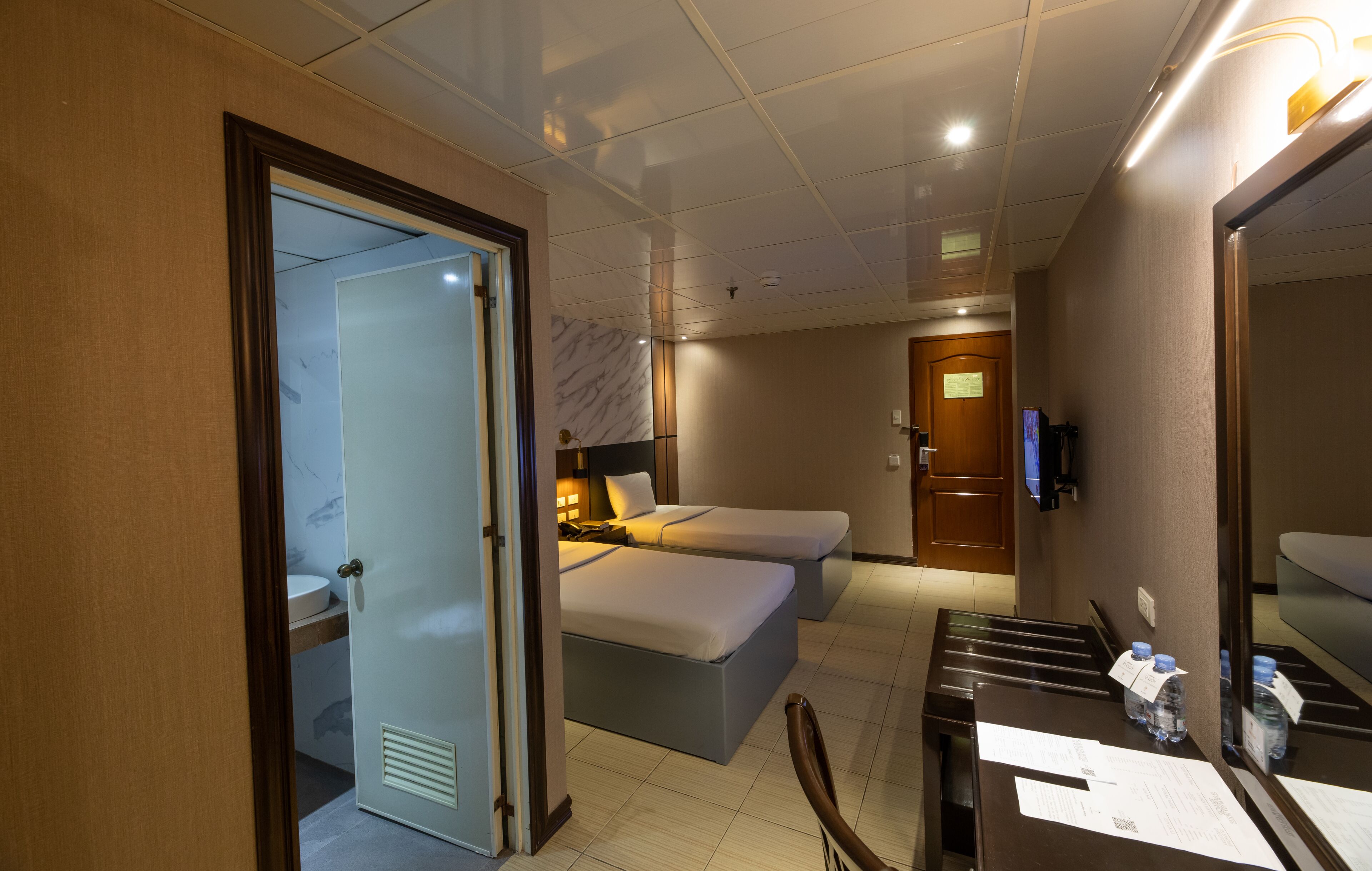 A hotel room with a bed, bedside table, chair, and a TV.
