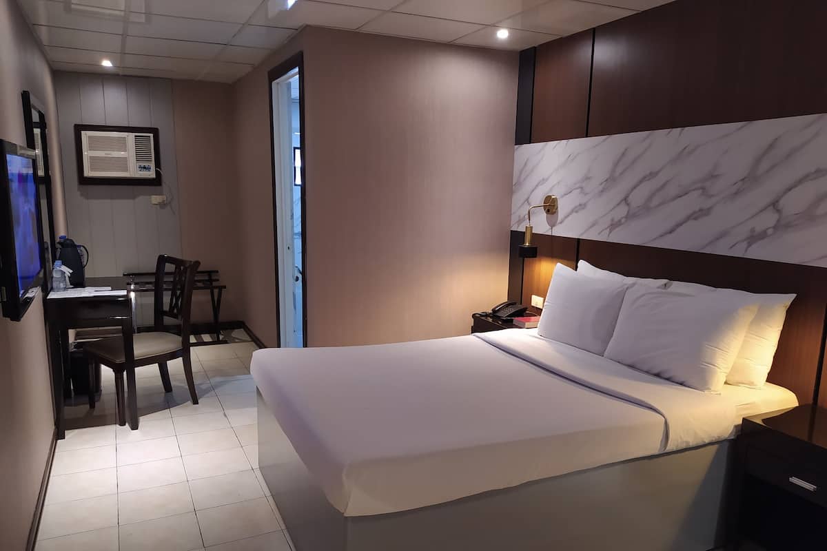 Una habitación de hotel con una cama grande, un escritorio con silla, un teléfono y aire acondicionado instalado en la pared.