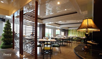 Uma sala de jantar ampla, com várias mesas e cadeiras, um pinheiro de Natal e um abajur decorativo grande.