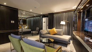 Una habitación de hotel moderna con sofá, sillones, televisión y minibar.