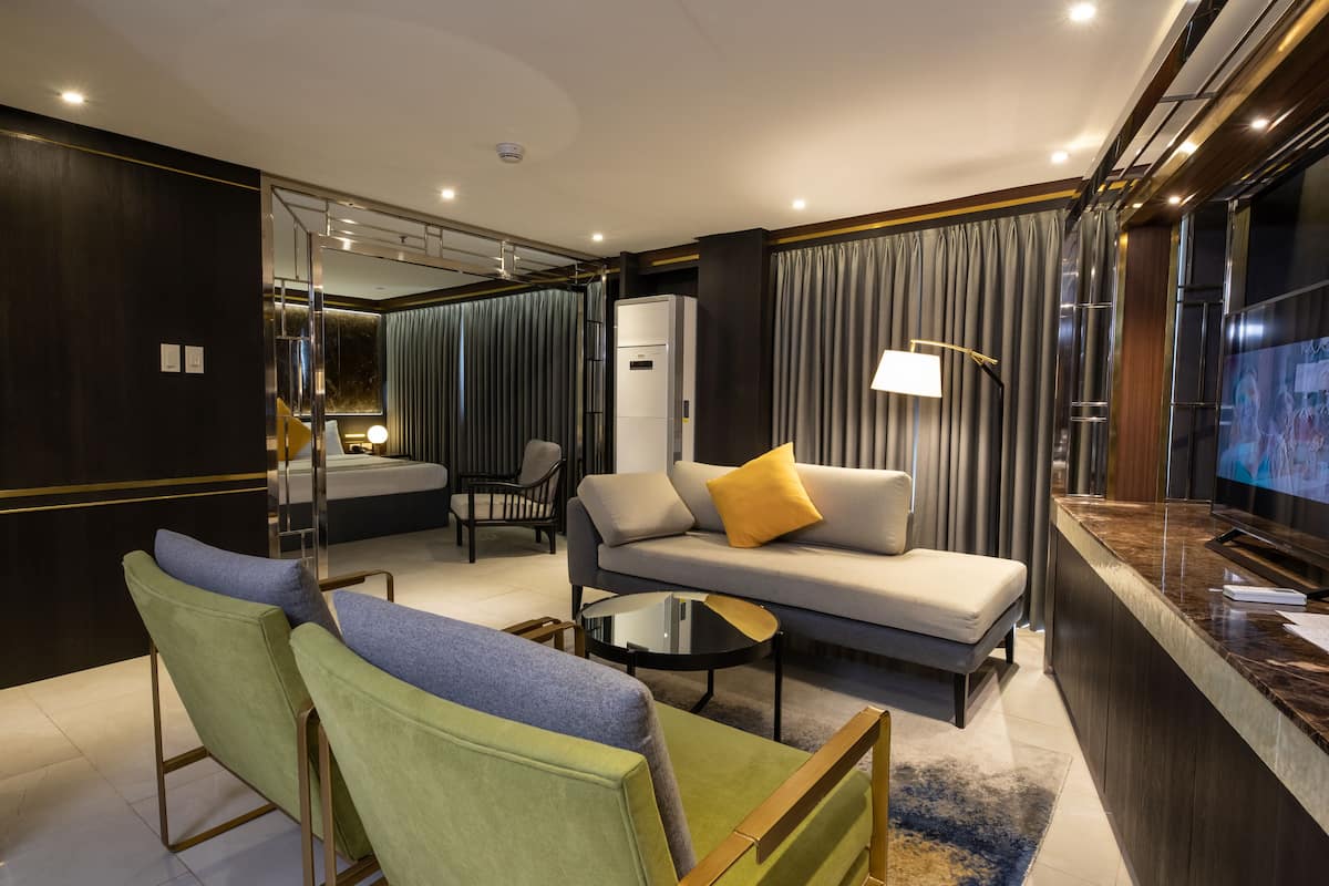 Una habitación de hotel moderna con sofá, sillones, televisión y minibar.