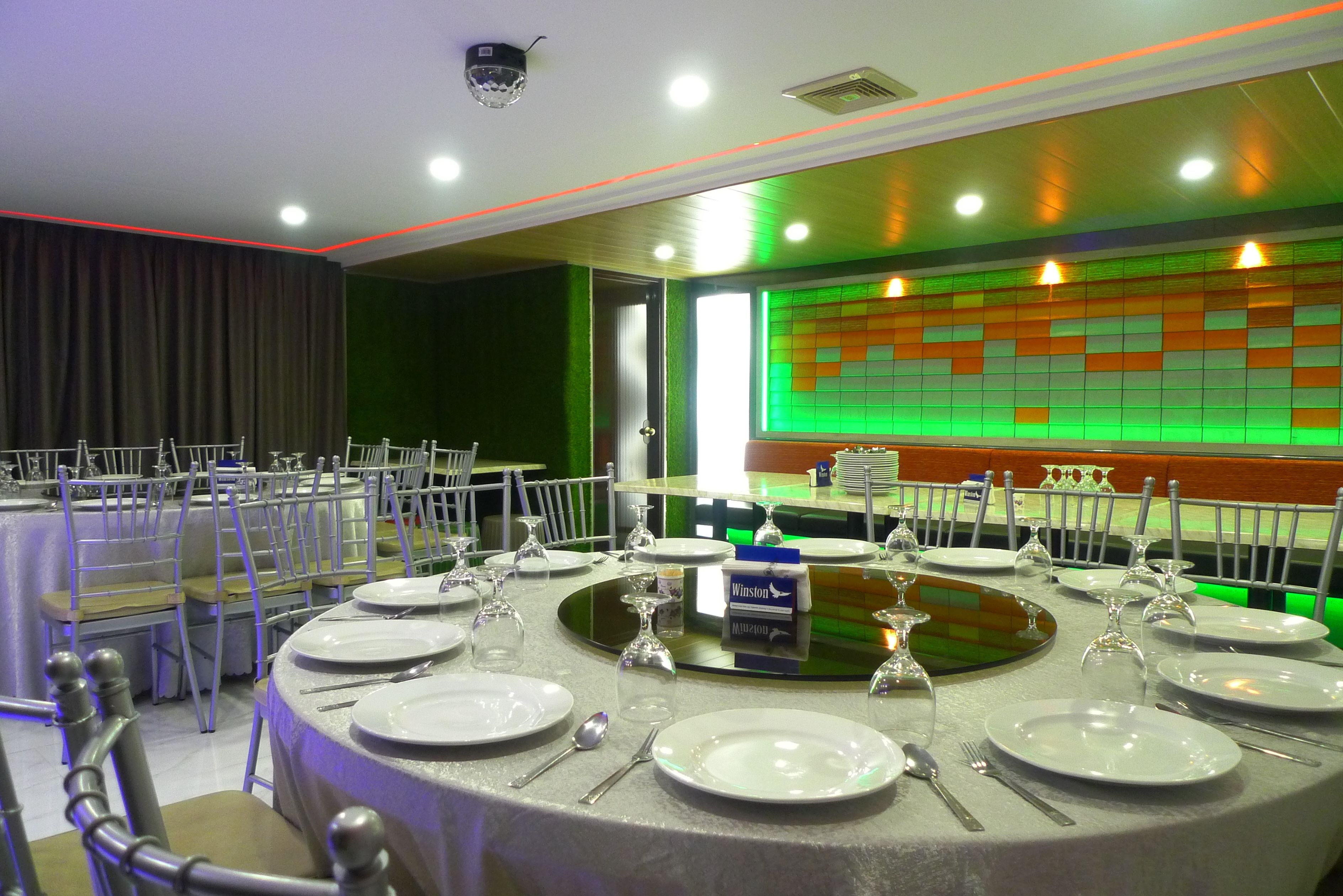 A banquet hall with round tables set for dining, equipped with plates, cutlery, and wine glasses.