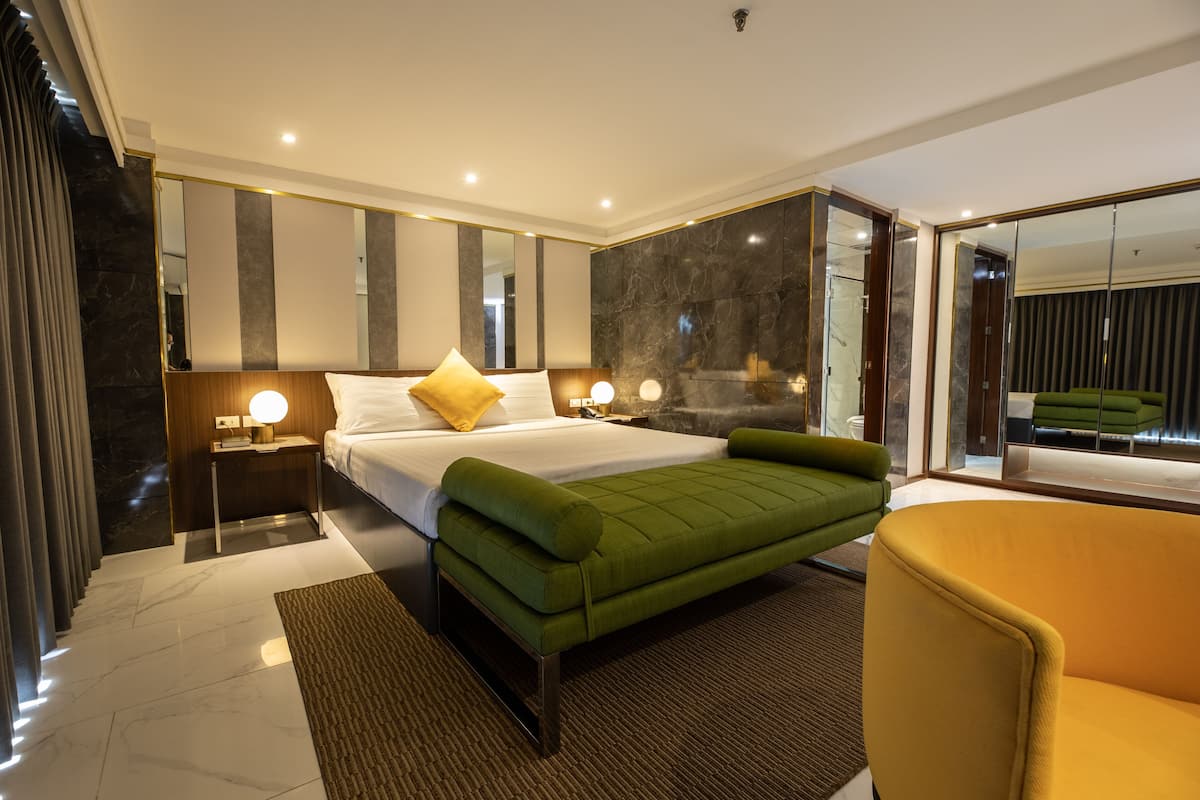 Un dormitorio moderno con una cama grande, lámparas de noche, un sofá verde y un espejo.