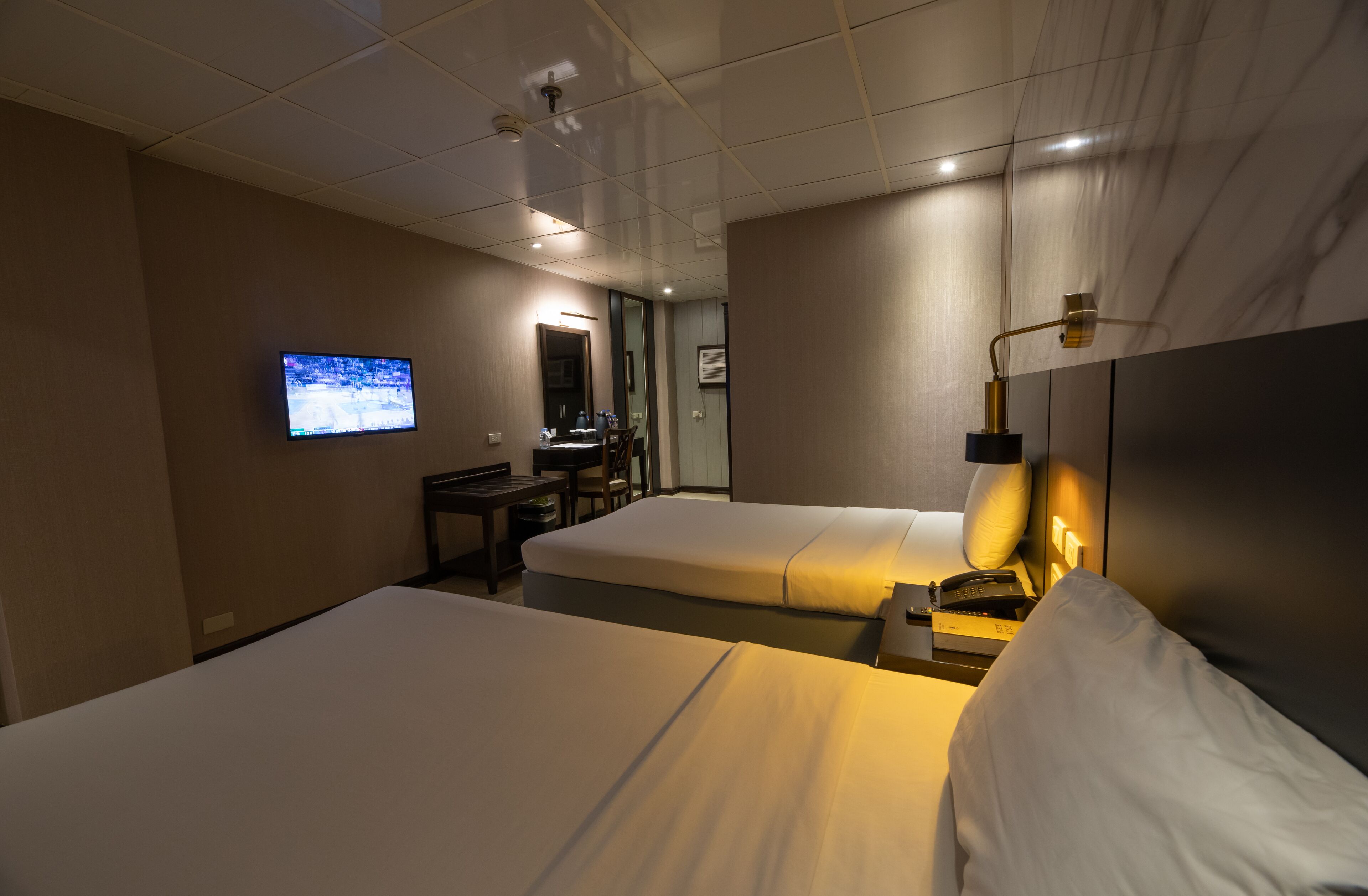A hotel room with two beds, a TV mounted on the wall, a desk with a chair, and a mirror.