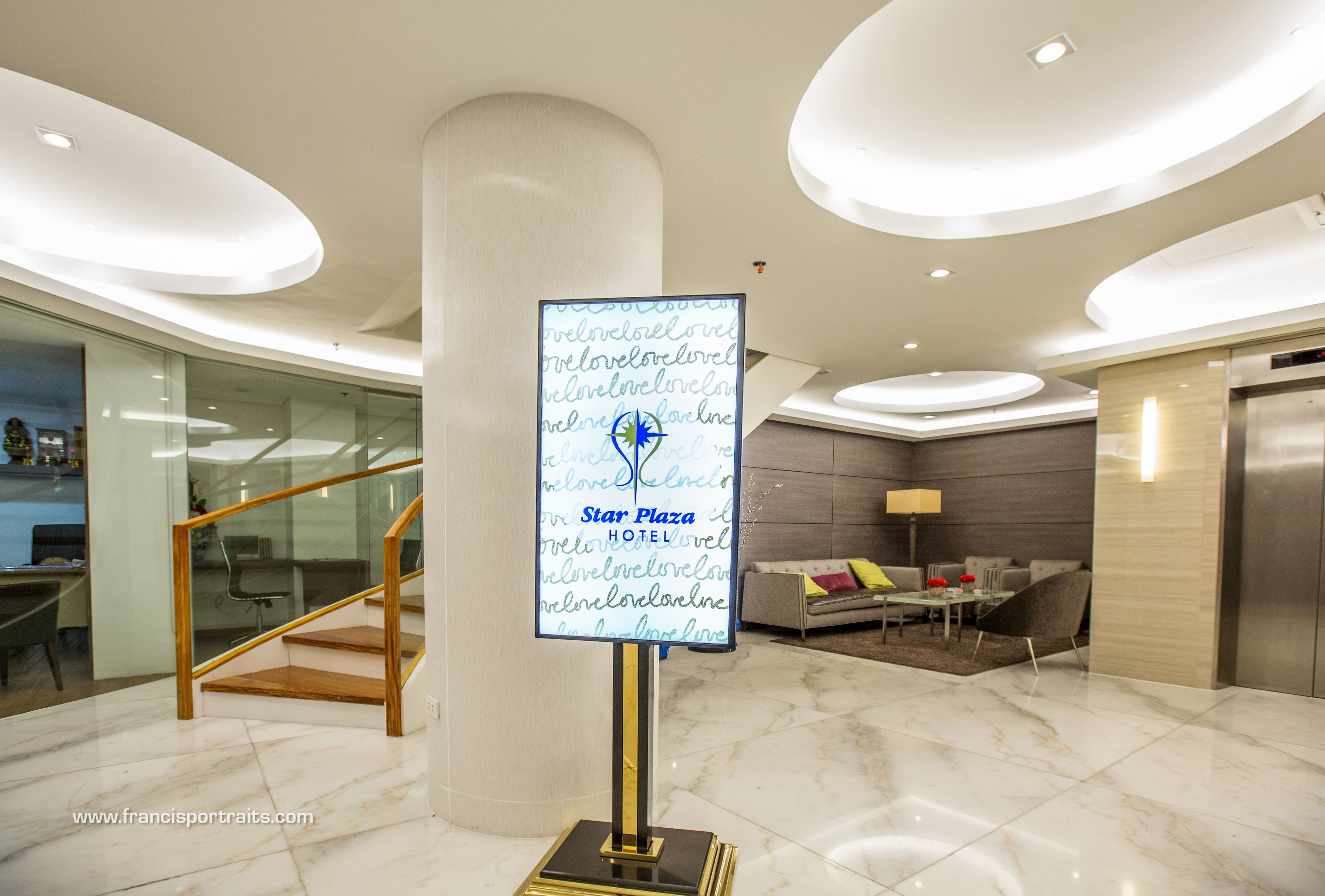 A modern hotel lobby with a marble floor, a staircase, a reception desk, and a seating area with a sofa and a coffee table.