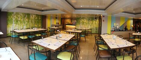 Un restaurante amplio con varias mesas y sillas, una zona de bar y un mural en la pared.