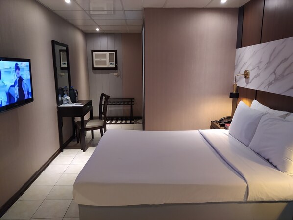 Habitación de hotel con cama, escritorio, silla, televisor y aire acondicionado instalado en la pared.