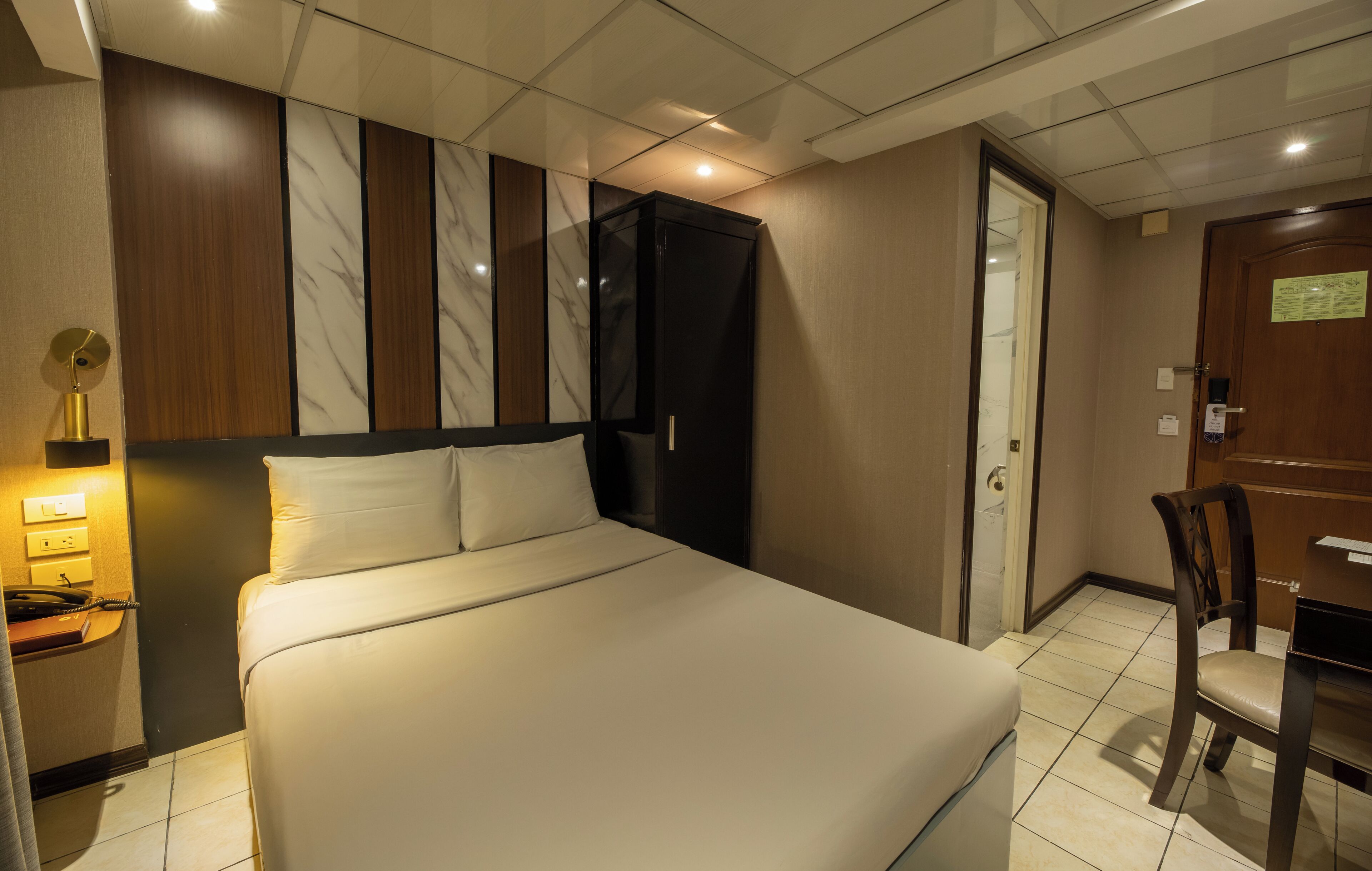 Habitació d'hotel amb un llit gran, un escriptori amb cadira, un armari i una làmpada de nit.