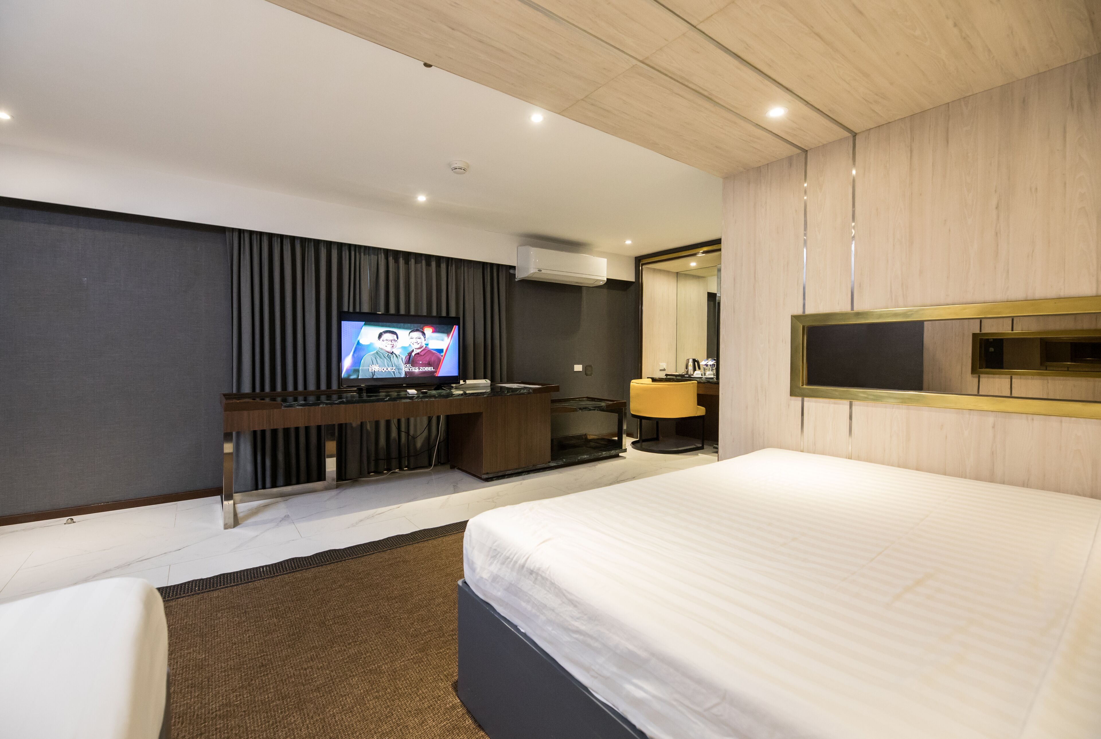 Una habitación de hotel moderna con una cama grande, un televisor de pantalla plana, un escritorio con una computadora y un espejo.