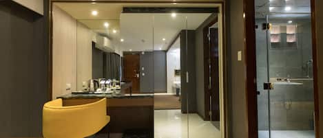 Une chambre d’hôtel moderne dotée d’une douche à parois de verre, d’un coin repas avec une chaise jaune et d’une cuisine ouverte.
