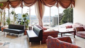 A spacious living area with a sofa, armchairs, and a coffee table. Large windows offer a view of the cityscape. - Nagasaki Sky Hotel (Nagasaki)