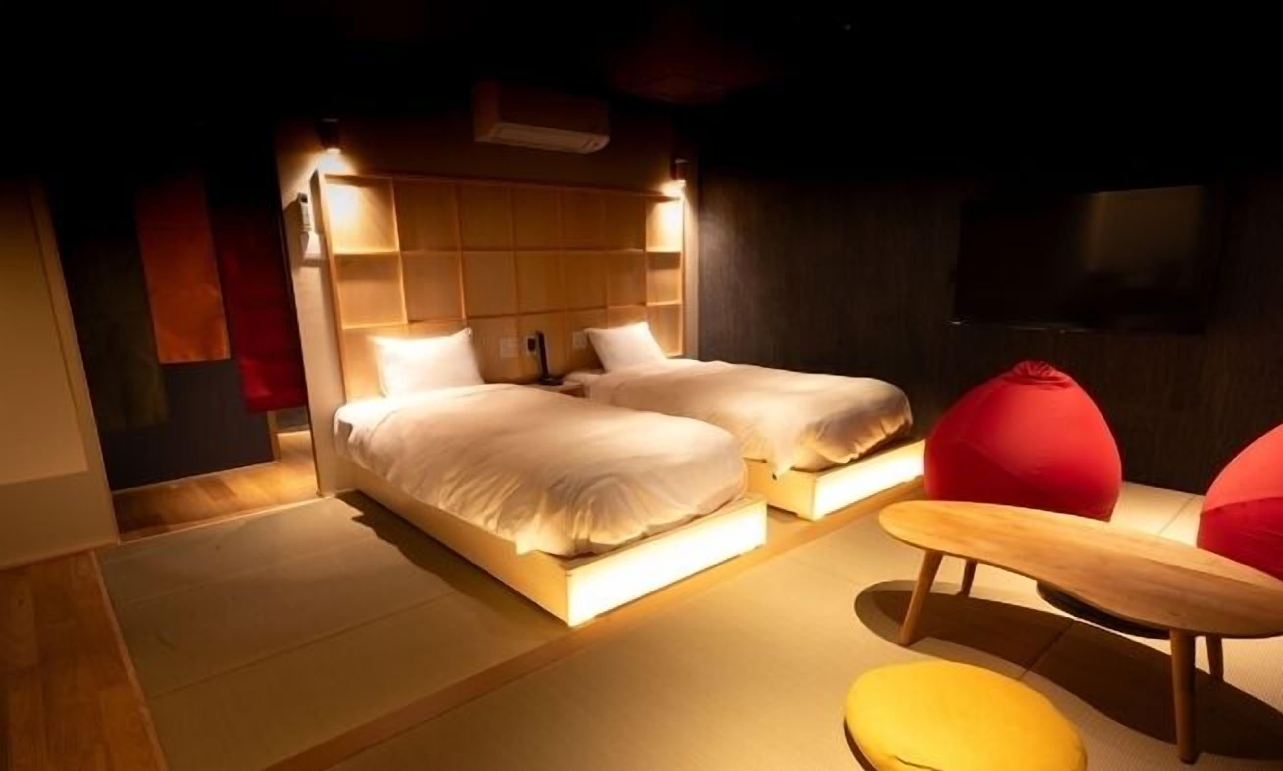 A modern hotel room with two beds, a small table, and a red chair.
