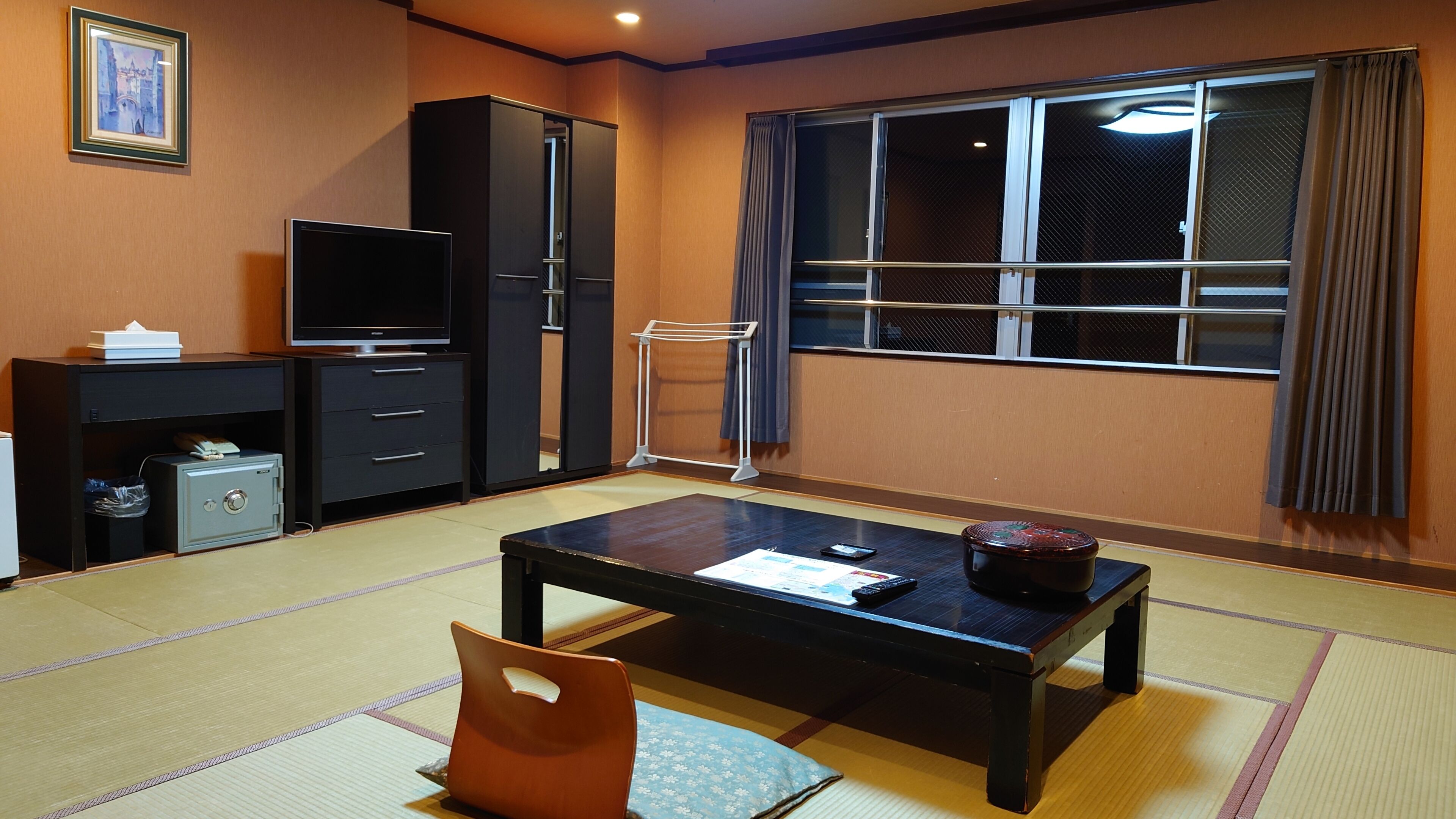 A room with tatami flooring, a black TV stand, a cabinet, a window with curtains, and a traditional Japanese table.