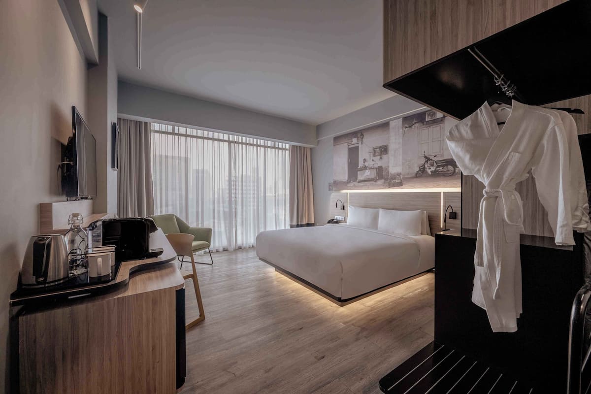 A modern hotel room with a large bed, a desk with a coffee maker, a chair, and a robe hanging on a rack.