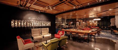 A spacious, well-lit lounge area with modern furniture, a bar, and a wall displaying various items.