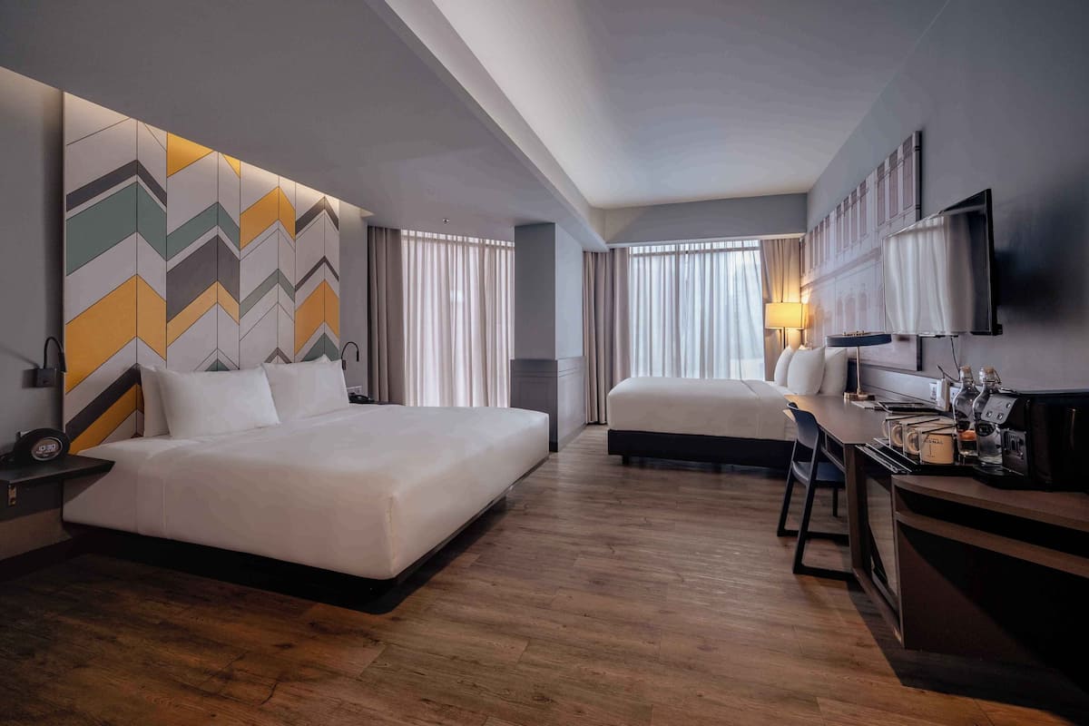 A hotel room with a large bed, a desk, a chair, a TV, and a wall with a geometric pattern.
