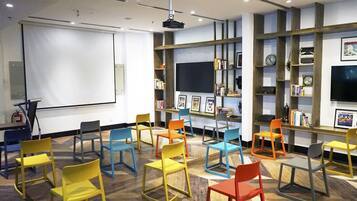 A conference room with a projector screen, multiple chairs, a bookshelf, and a television.