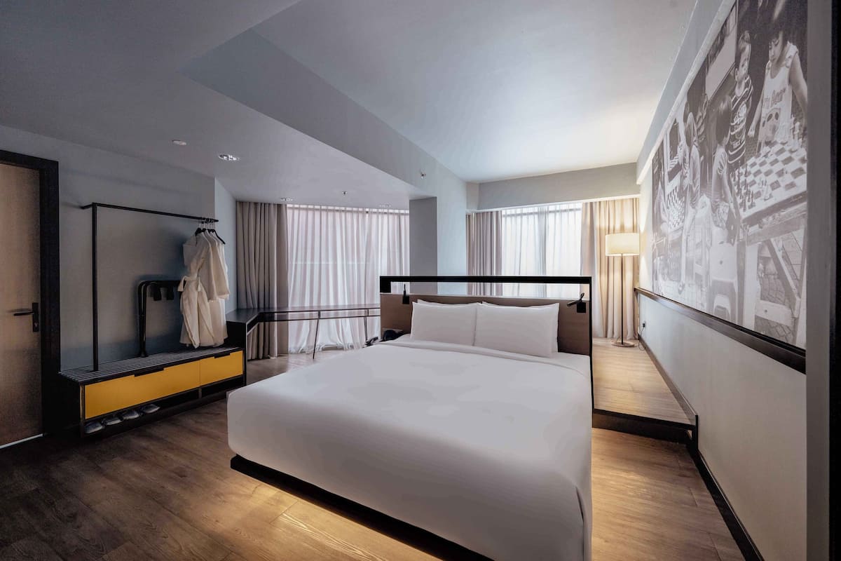 A modern hotel room with a large bed, a walk-in closet, and a large window with curtains.