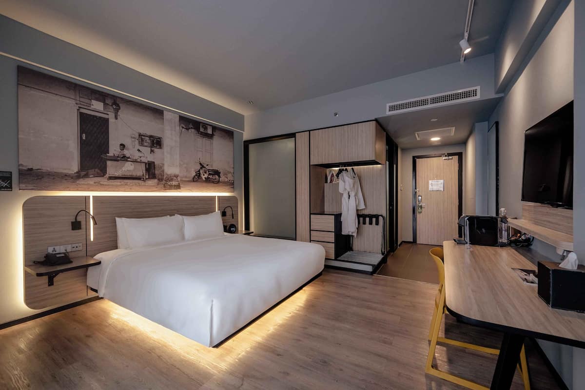 A modern hotel room with a large bed, a desk, and a wardrobe.