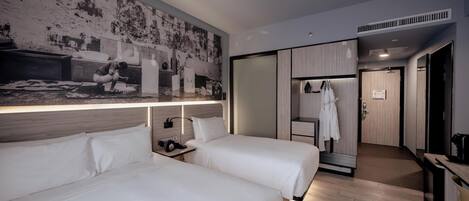 A hotel room with two beds, a large wall mural, a desk with a chair, and a walk-in closet.