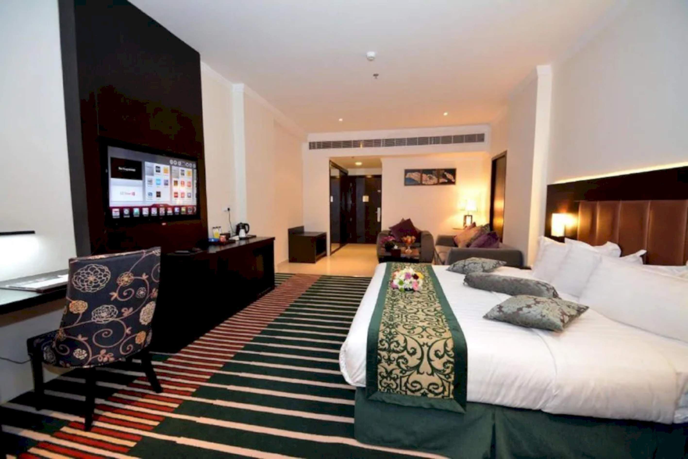 A hotel room with a bed, a desk with a computer, a TV, and a chair.