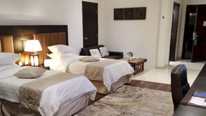 Habitación de hotel con dos camas, un escritorio, una silla, una lámpara y un adorno en la pared.
