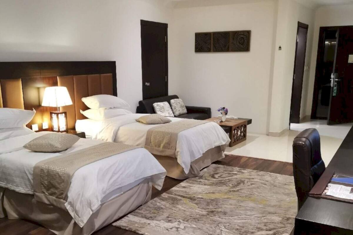 Habitación de hotel con dos camas, un escritorio, una silla, una lámpara y un adorno en la pared.