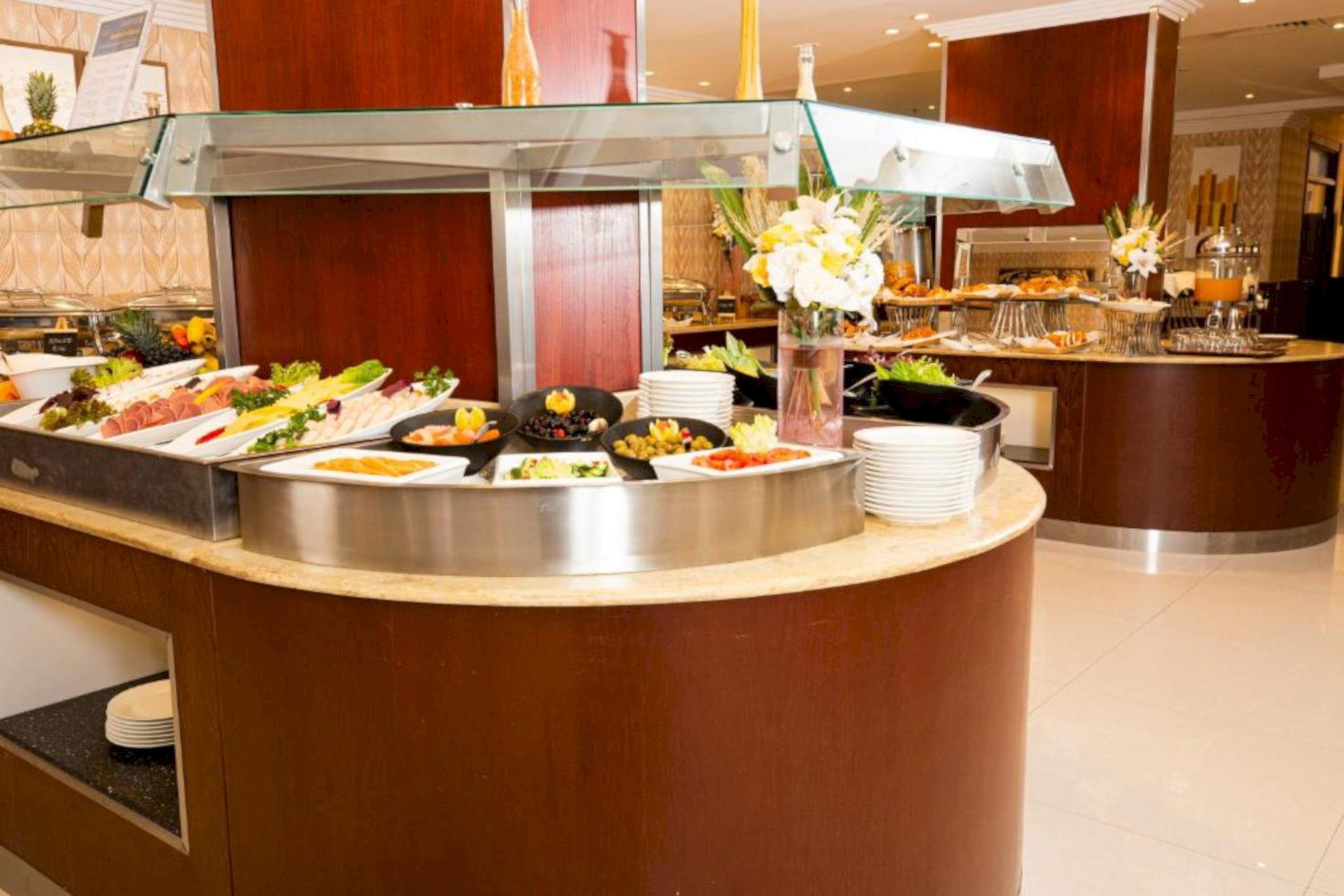 En buffet med forskellige madstationer, herunder frugt, salat og varme retter, anrettet på en disk med en glasmontre.