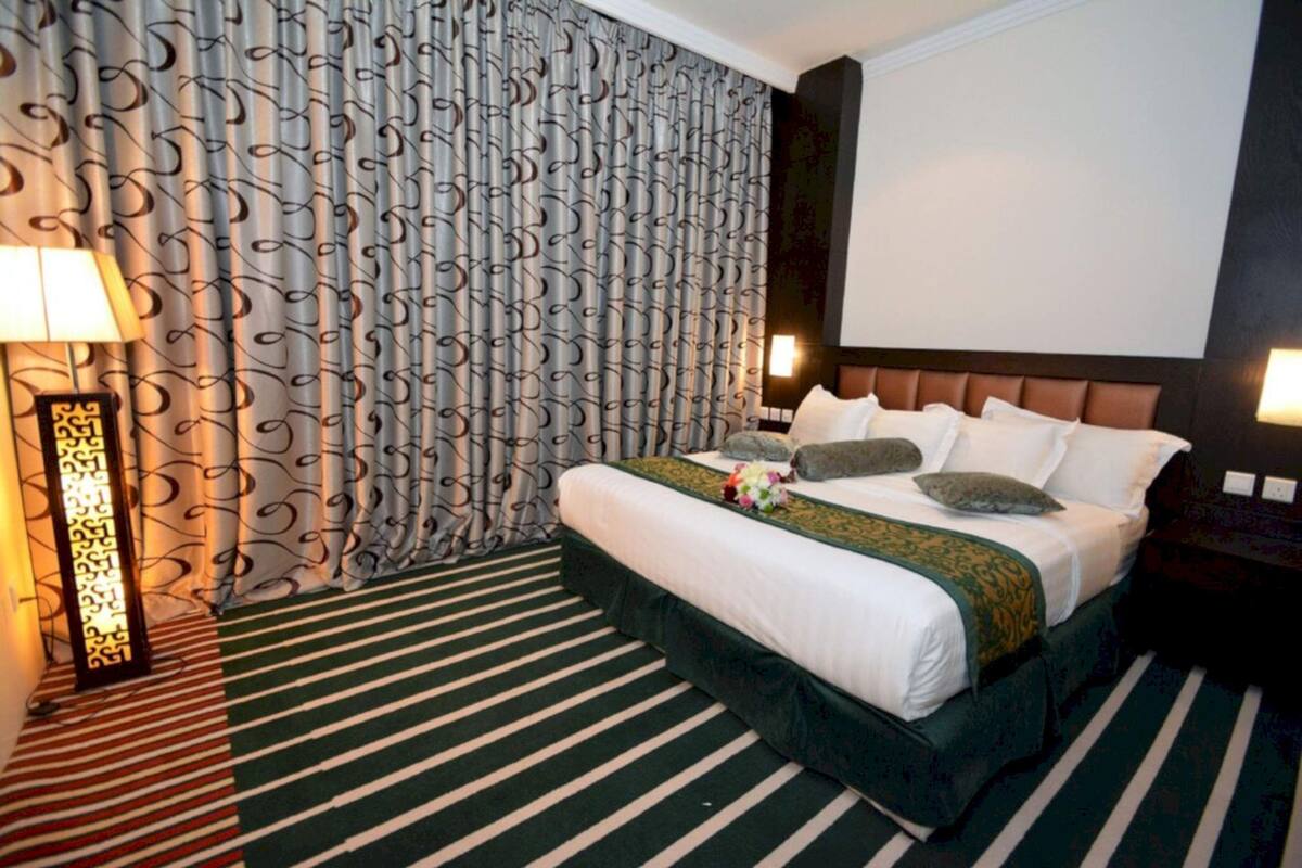 Una habitación de hotel con cama, cortina estampada, alfombra a rayas y televisor montado en la pared.