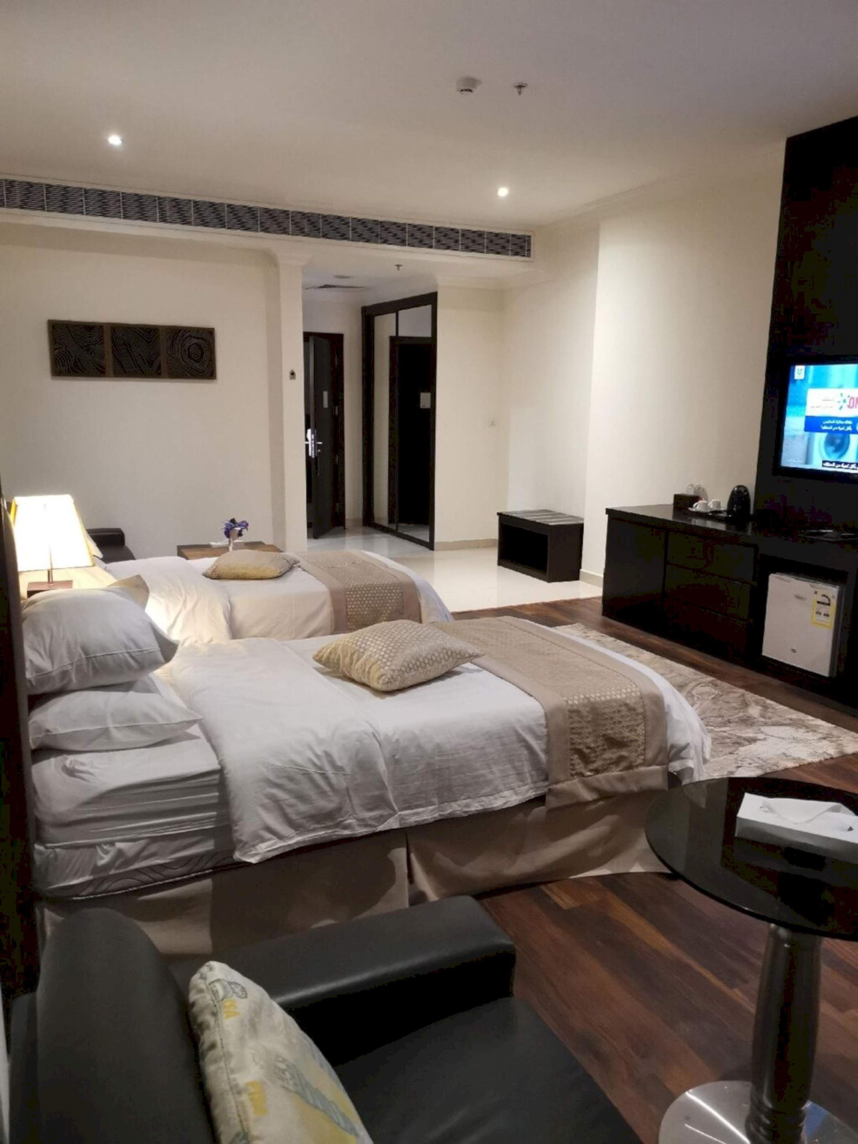 A hotel room with two beds, a desk, a TV, and a small kitchenette.