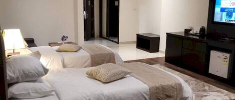 A hotel room with two beds, a desk, a TV, and a small kitchenette.