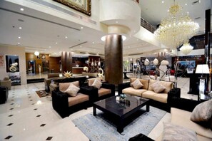 Un hall d’entrée spacieux avec un plafond haut, un grand lustre et un coin salon comprenant des canapés et une table basse.
