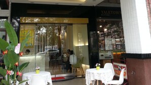 The exterior of Travel Young Hotel with a modern facade, a glass entrance, and outdoor seating area. - Travel Young (Kaohsiung)
