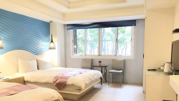 A hotel room with a large bed, a smaller bed, a desk with a chair, a television, and a window with a view of trees. - Travel Young (Kaohsiung)