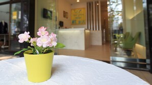 A yellow flower pot with pink flowers on a white tablecloth in a modern interior space with glass walls and a reception area in the background. - Travel Young (Kaohsiung)