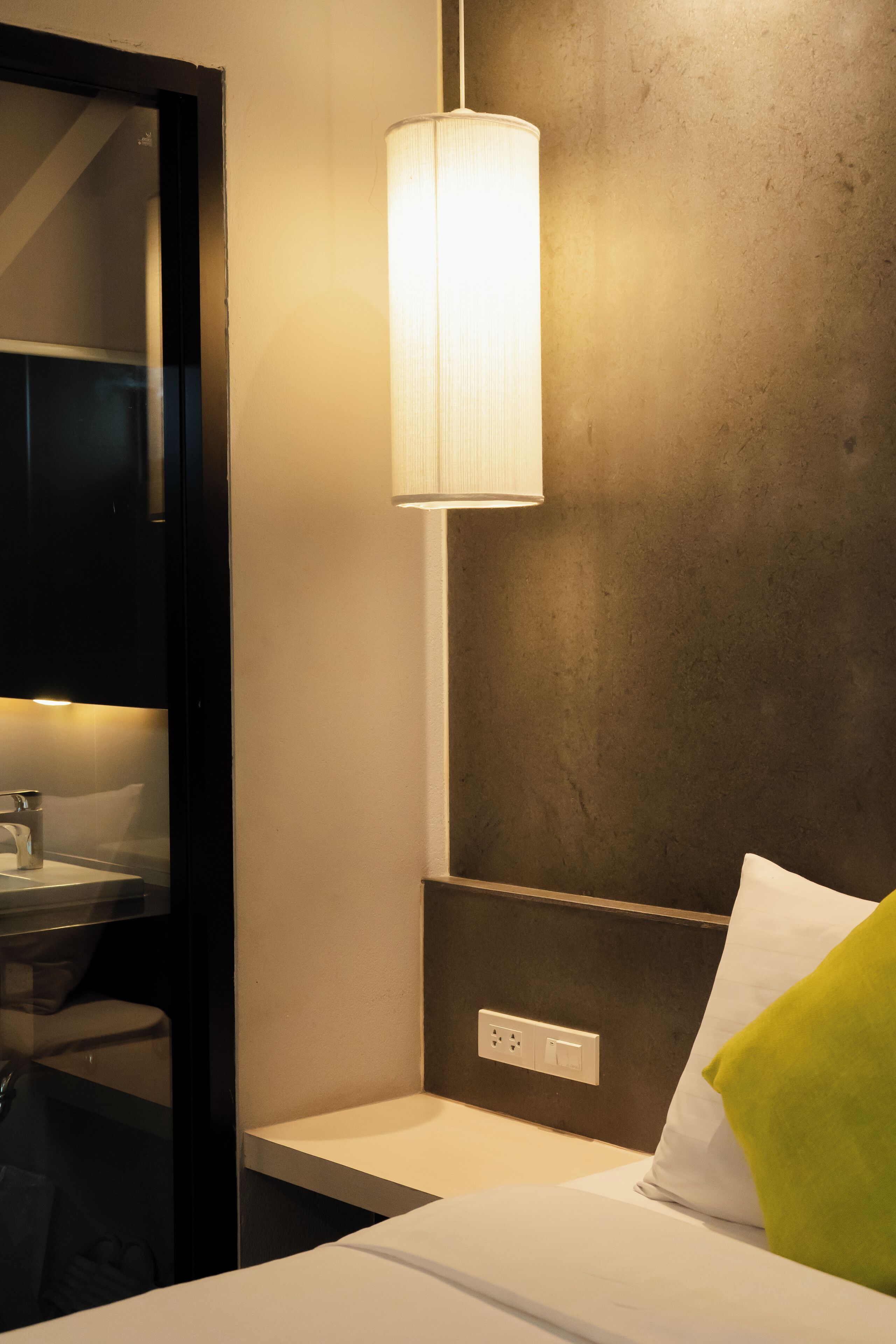 A hotel room with a bed, a nightstand, a lamp, and a wall socket.