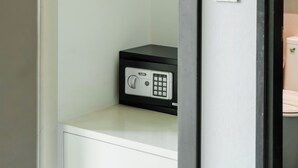 Habitación compacta con un armario blanco, un dispositivo electrónico negro encima y un perchero de madera en la pared.