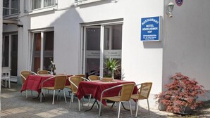 Un área de estar al aire libre con mesas y sillas, un letrero para restaurante y hotel, y una planta en maceta.