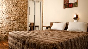 A bedroom with a large bed, a stone wall, a wooden door, and a small table with a lamp. - Marble Tower Hotel (Beirut)