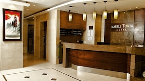 A hotel reception area with a marble counter, wooden cabinets, and hanging pendant lights. - Marble Tower Hotel (Beirut)