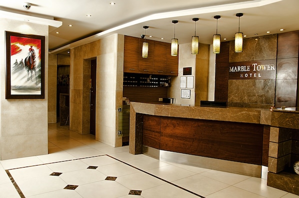 A hotel reception area with a marble counter, wooden cabinets, and hanging pendant lights. - Marble Tower Hotel (Beirut)
