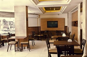 A restaurant with multiple tables and chairs, a flat-screen TV mounted on the wall, and a view of the street outside. - Marble Tower Hotel (Beirut)