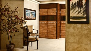 A lobby with a wooden wardrobe, a chair, a potted plant, and a painting. - Marble Tower Hotel (Beirut)