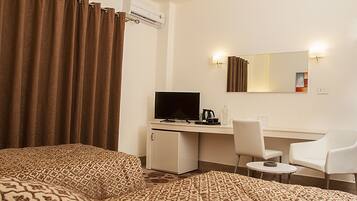 A hotel room with a bed, a desk with a computer, a chair, and a small table.