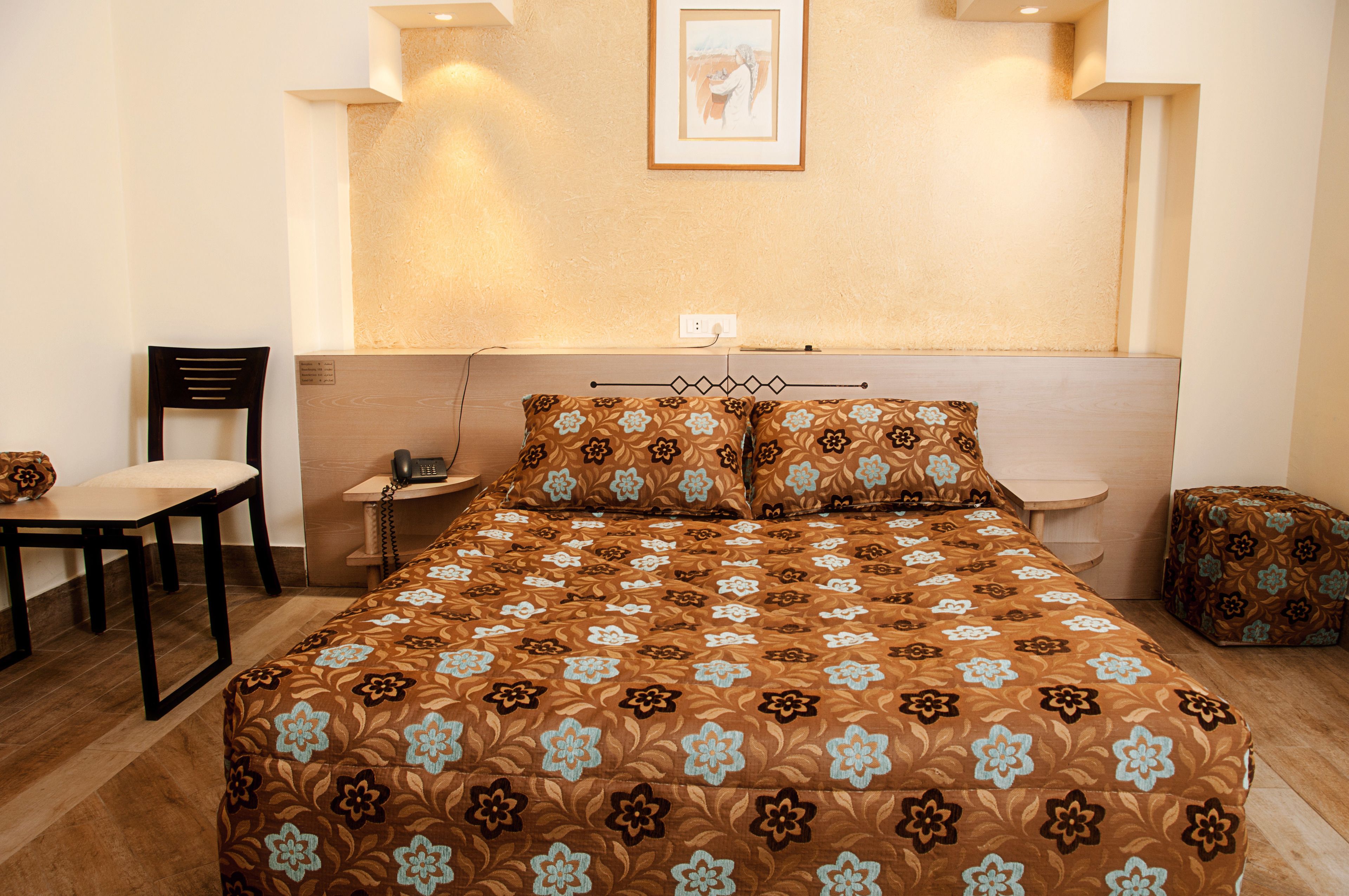 A neatly arranged bedroom with a bed, a chair, a bedside table, and a small table with a telephone.
