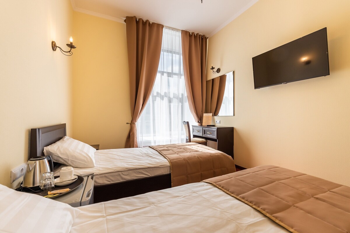 A hotel room with two beds, a flat-screen TV, a desk with a lamp, and a window with curtains.