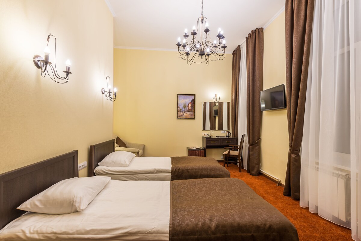 A hotel room with two beds, a chandelier, a TV, and a desk.