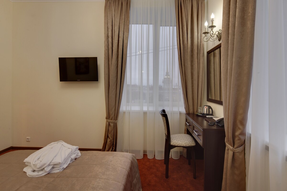 A hotel room with a bed, a desk with a chair, a television, and a window with curtains.